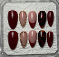 A set of 10 press-on nails displayed in a clear plastic case on textured white paper. The nails feature a mix of deep burgundy, dusty pink, metallic gold trim, and a dark red and black tortoiseshell pattern.