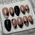 A set of 10 press-on false nails displayed in a clear plastic case on a textured white background. The nails feature a mix of dusty pink, glossy black, and white French tips with small gold star and heart accents.